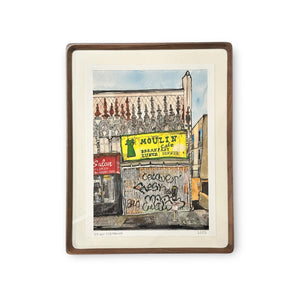 Framed print of a watercolor illustration with intricate architecture behind storefronts including a clear view of a yellow and green Moulin Cafe street billboard. 