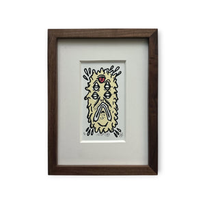 Cream colored Eye Gato Abductor character with black outline and red tongue on top. Mounted on white boards with a custom brown wood frame.