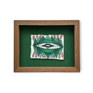 Brown walnut custom frame with green eye and red water drops on white rives paper while mounted on a textured green board.