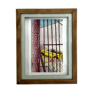 Framed watercolor still life art featuring a yellow truck viewed through a red fence.